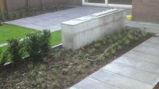 Strakke moderne tuin aan laten leggen in Breda. In deze tuin zijn de volgende materialen verwerkt. Schellevis tegels 50x100  Een strakke betonmuur met een rvs waterelement